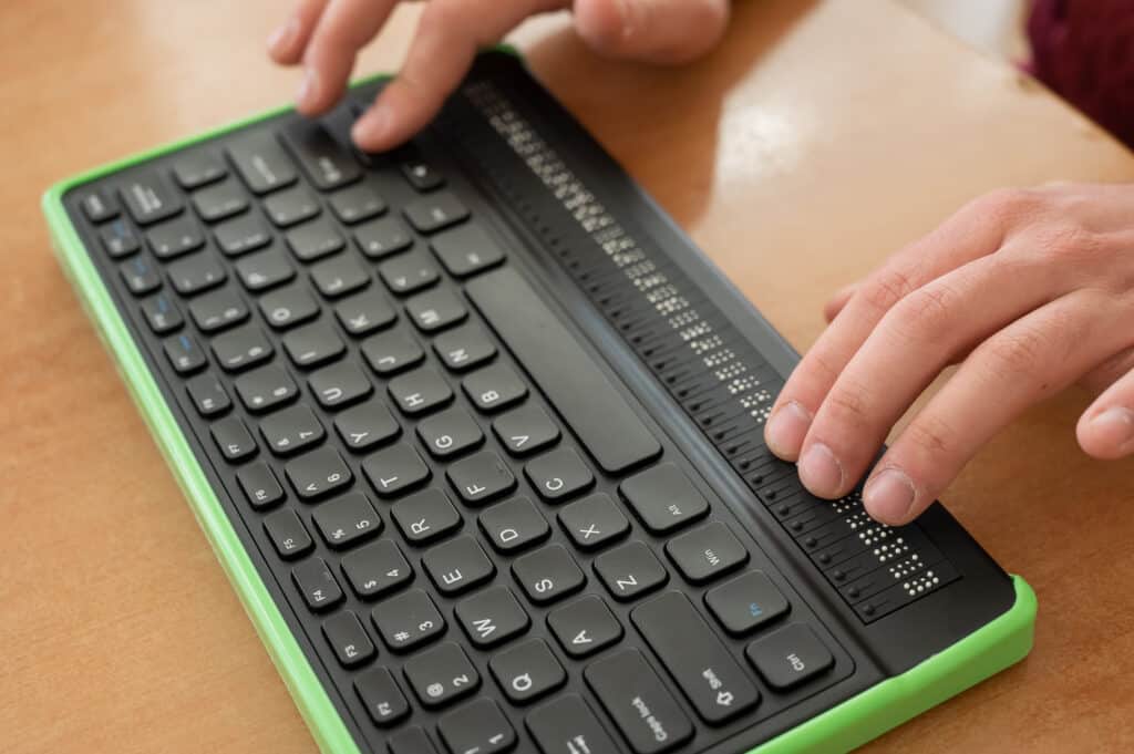 Ein blinder Mann benutzt einen Computer mit einer Braillezeile und einer Computertastatur. Inklusives Gerät